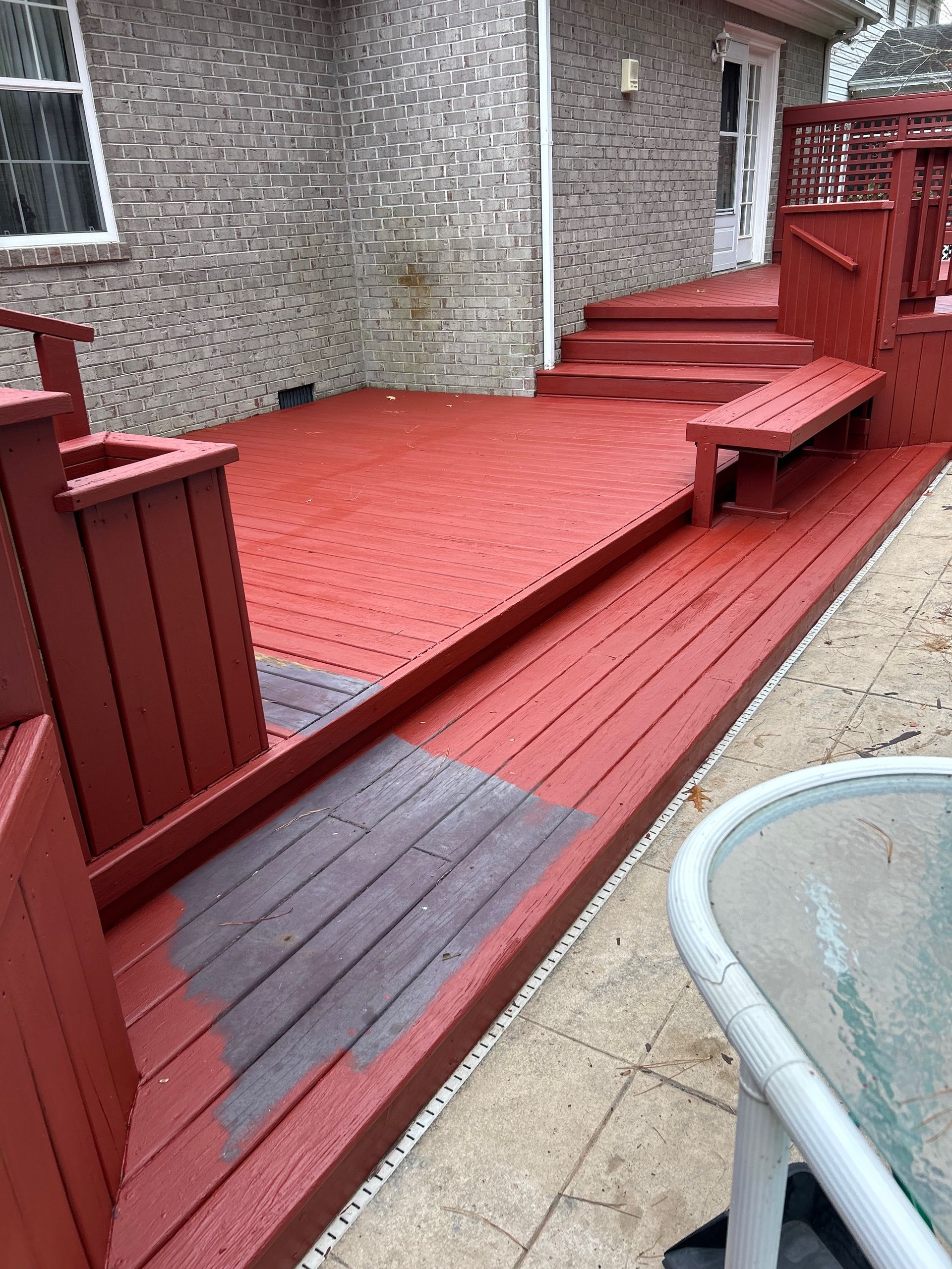 Red-painted accessible wooden deck ramp with steps beside a house, viewed from the patio.