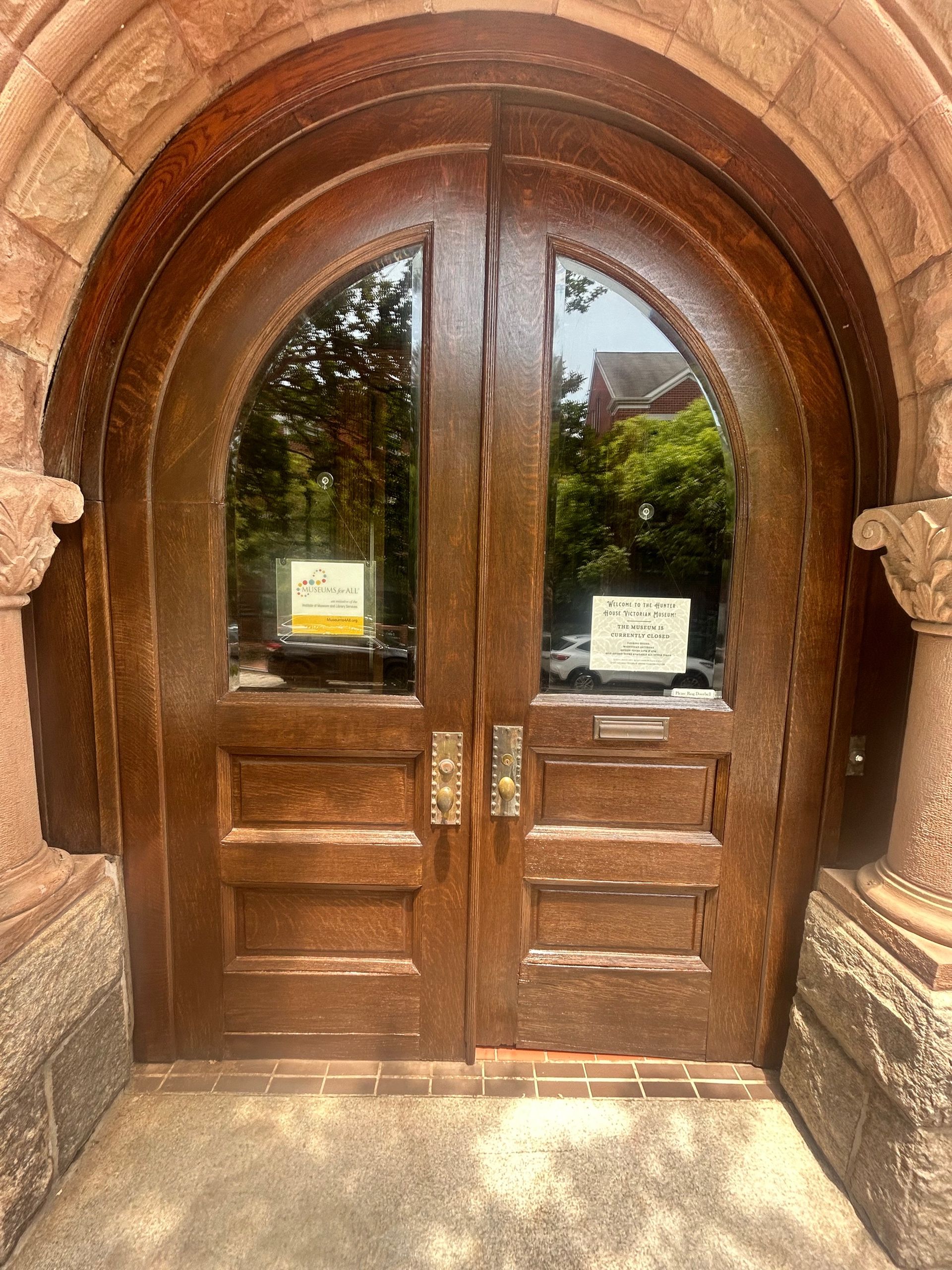 Arched wooden double doors with glass panes and posted notices at a building entrance
