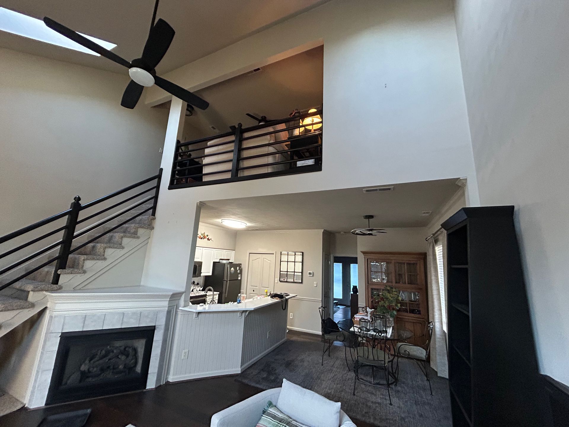 Open living room with staircase, fireplace, loft railing, and dining area under vaulted ceilings