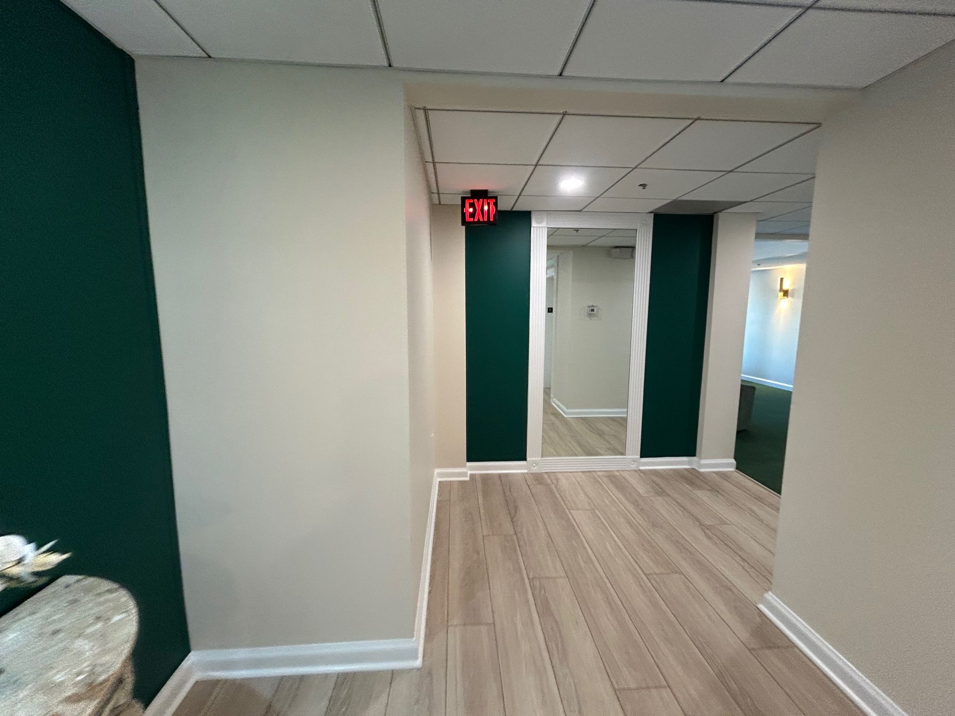 Empty hallway with wood-look flooring, white walls, green accents, and a mirrored elevator area