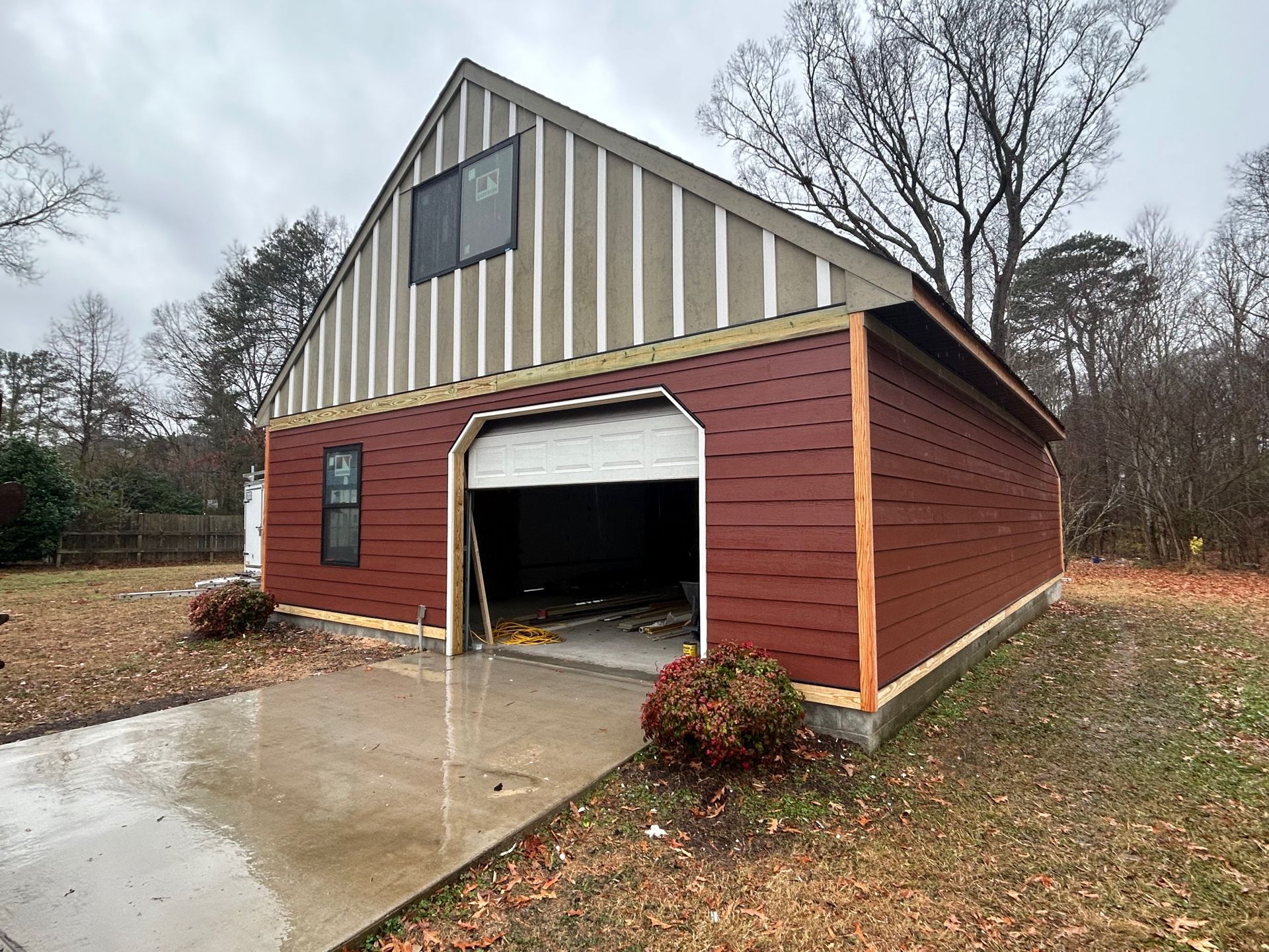 Red barn with open garage door and concrete driveway on a rainy, wooded property