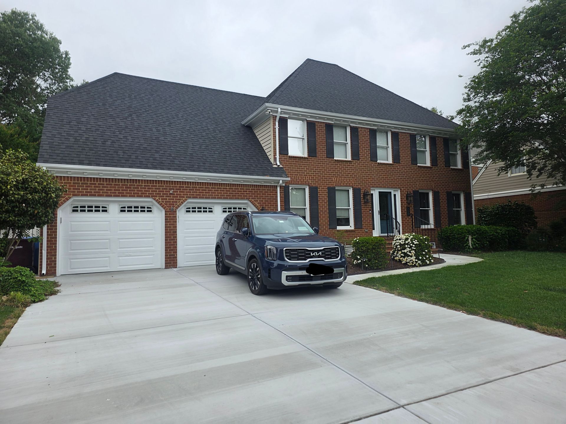 Two-story brick house with white garage doors and a black SUV in the driveway.