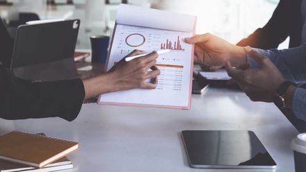 a group of people are sitting at a table looking at a graph .