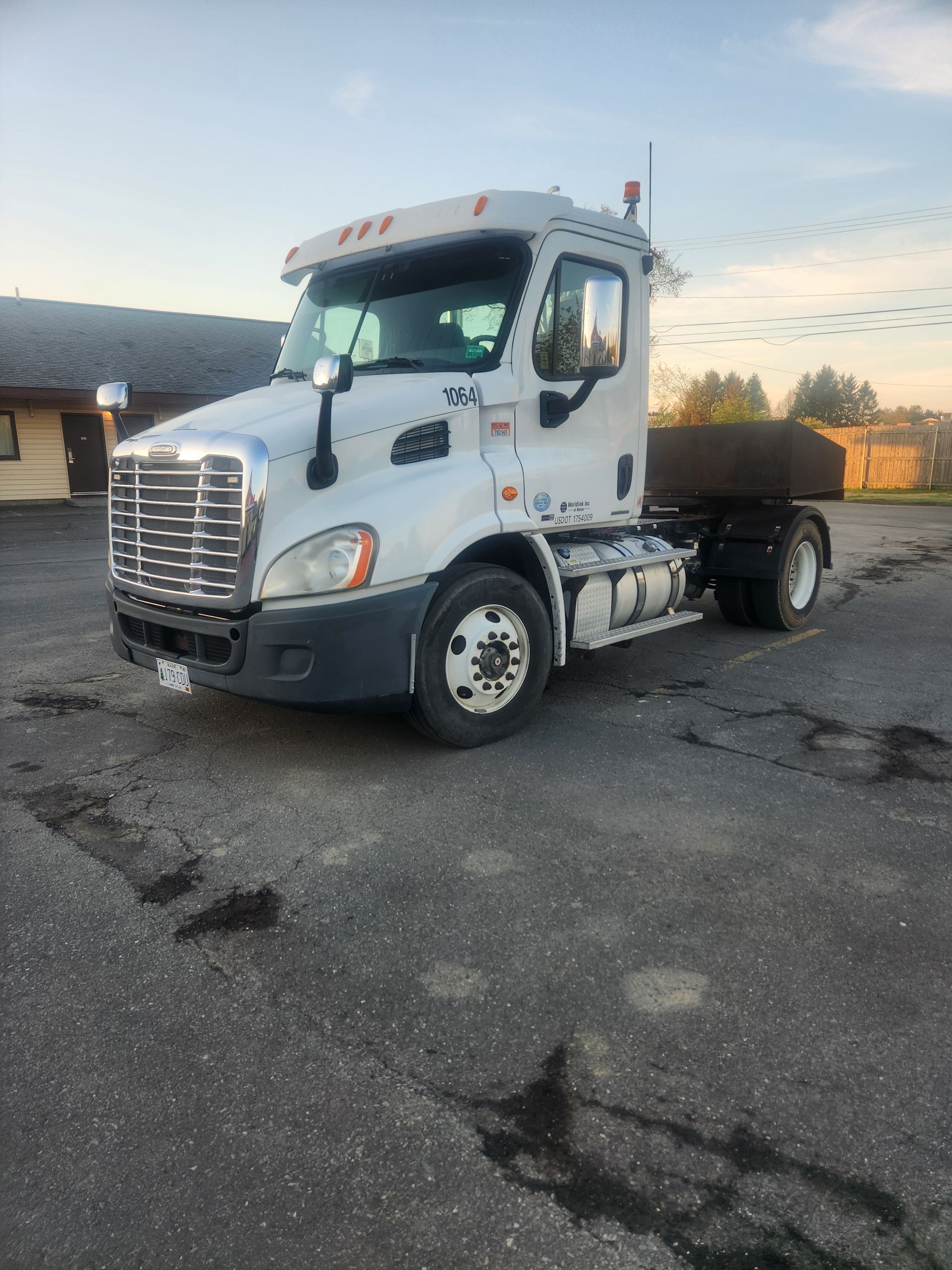 A white Freightliner semi-truck parked on an asphalt lot at sunset.
