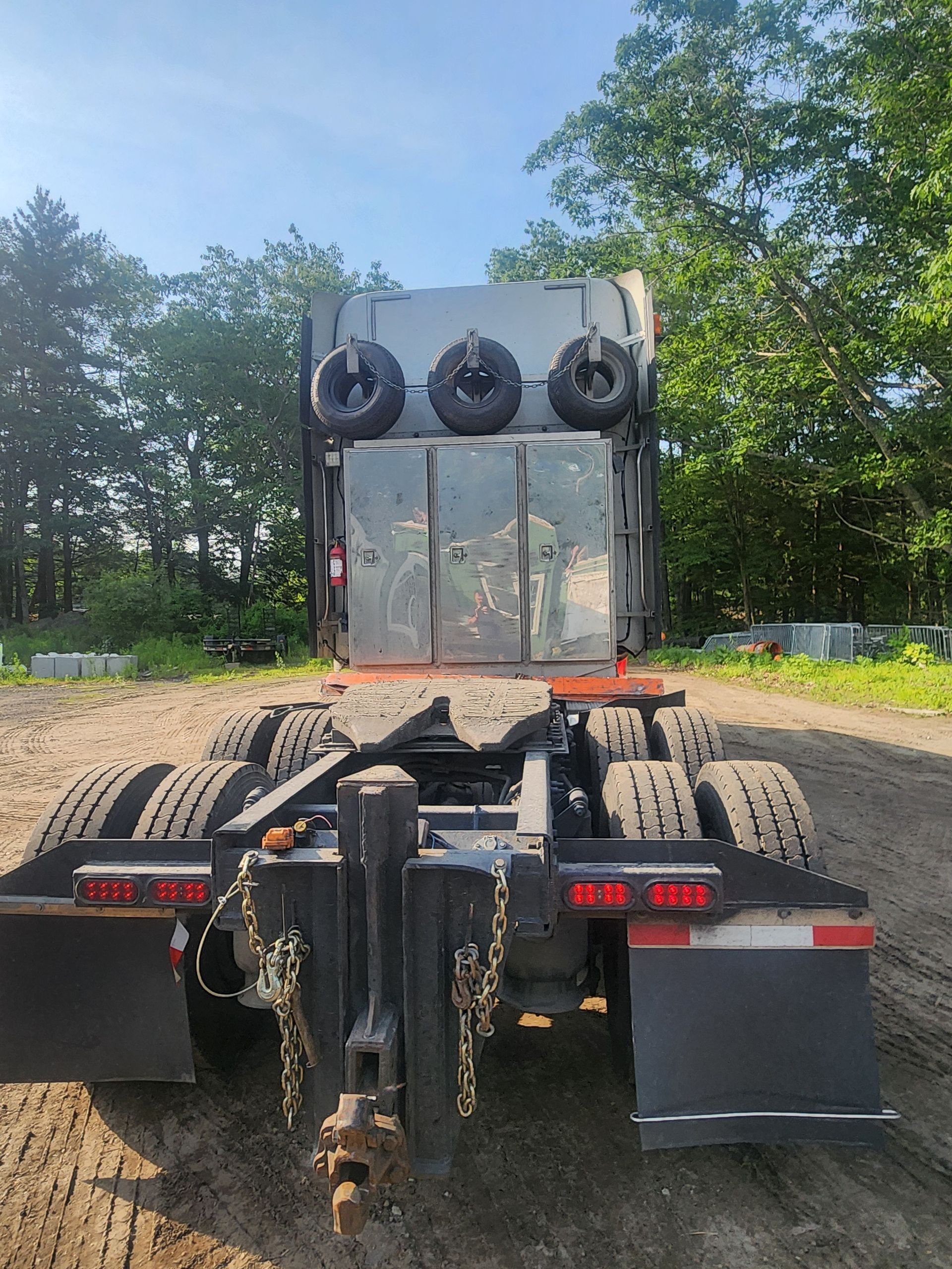 Rear view of a dark truck chassis parked on a dirt lot, featuring a headache rack with three spare tires.