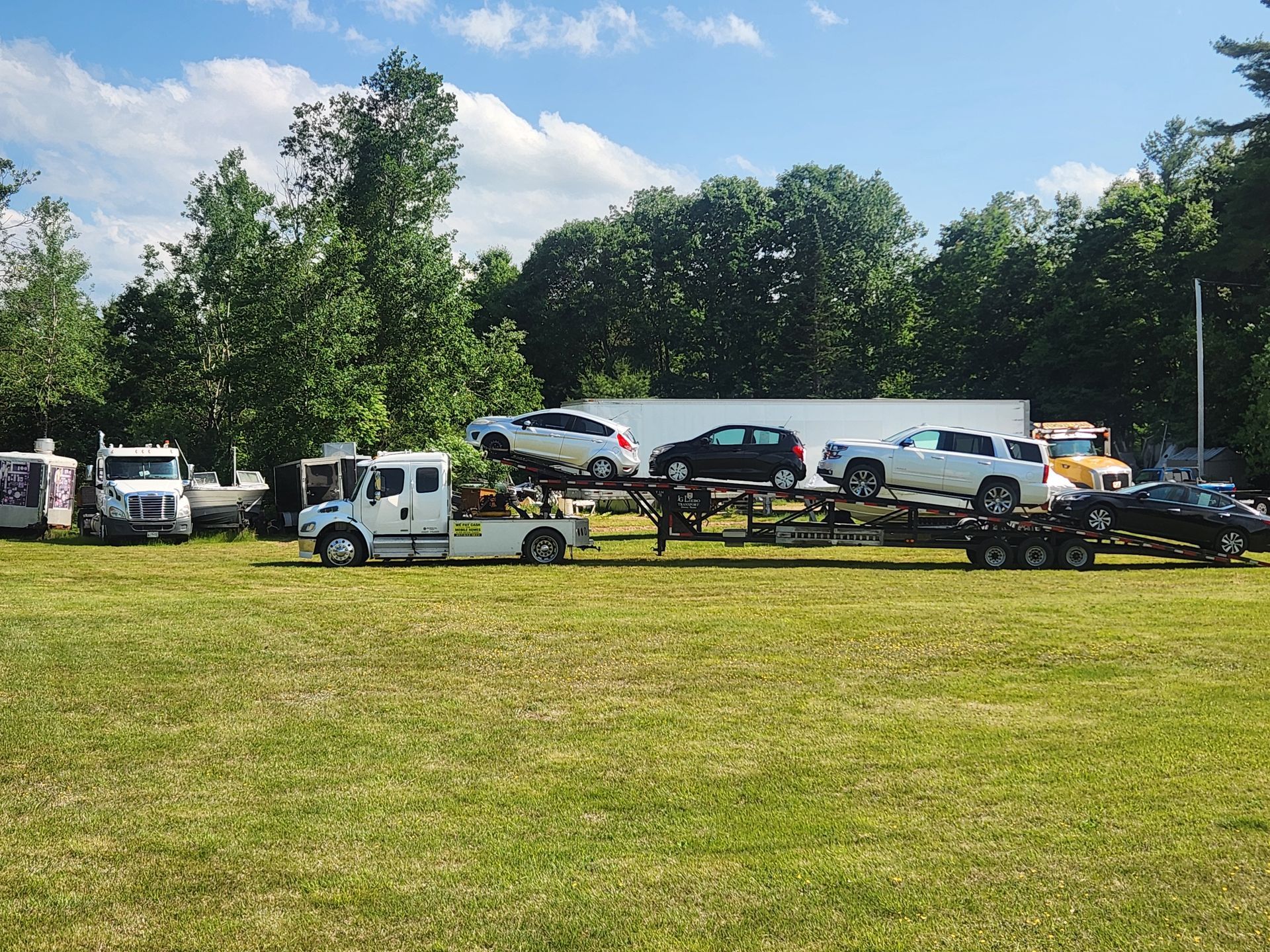 A white car carrier truck parked in a grassy field with several cars loaded on its trailer.
