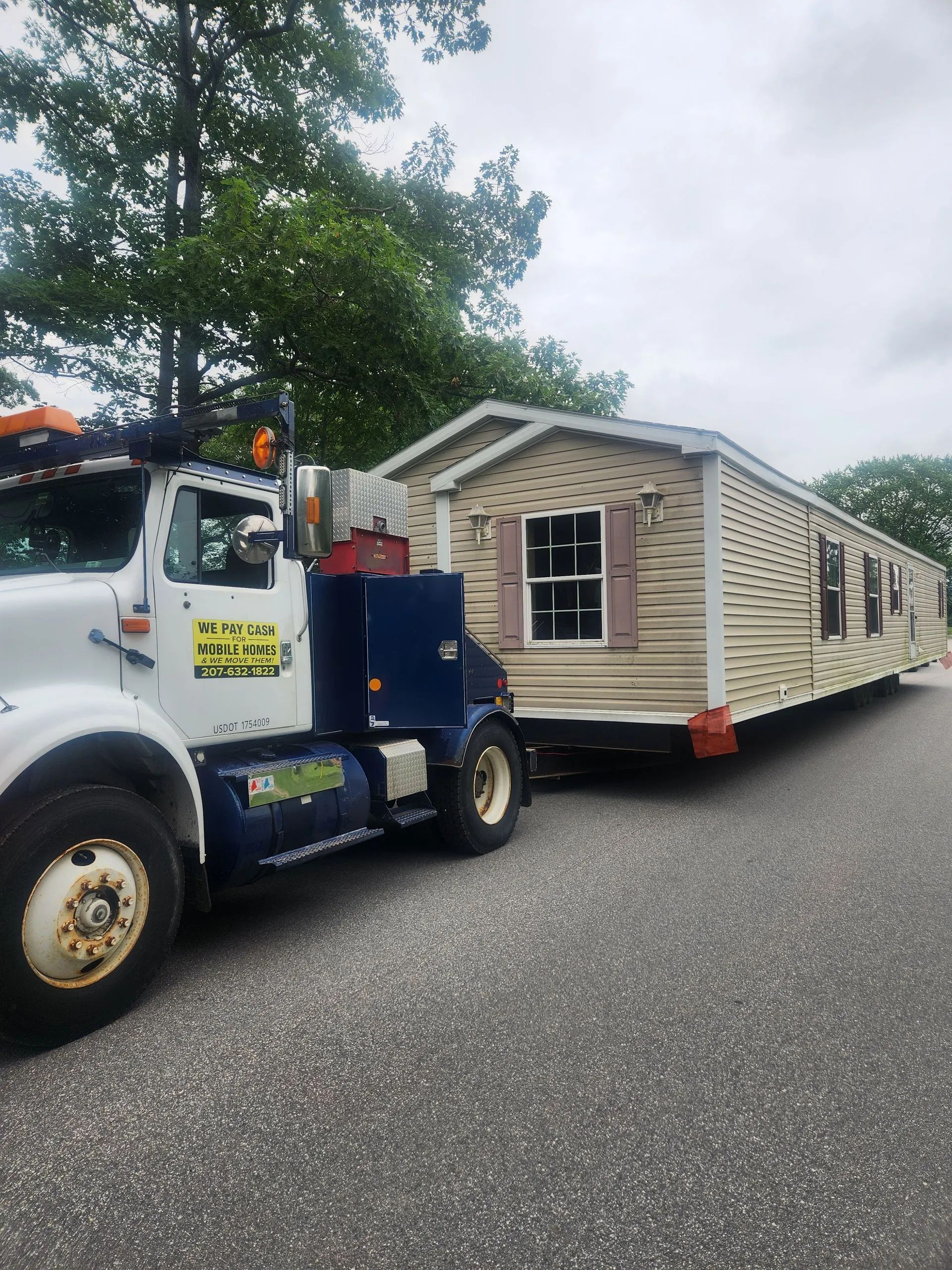 Tow truck towing a beige mobile home on a tree-lined residential street