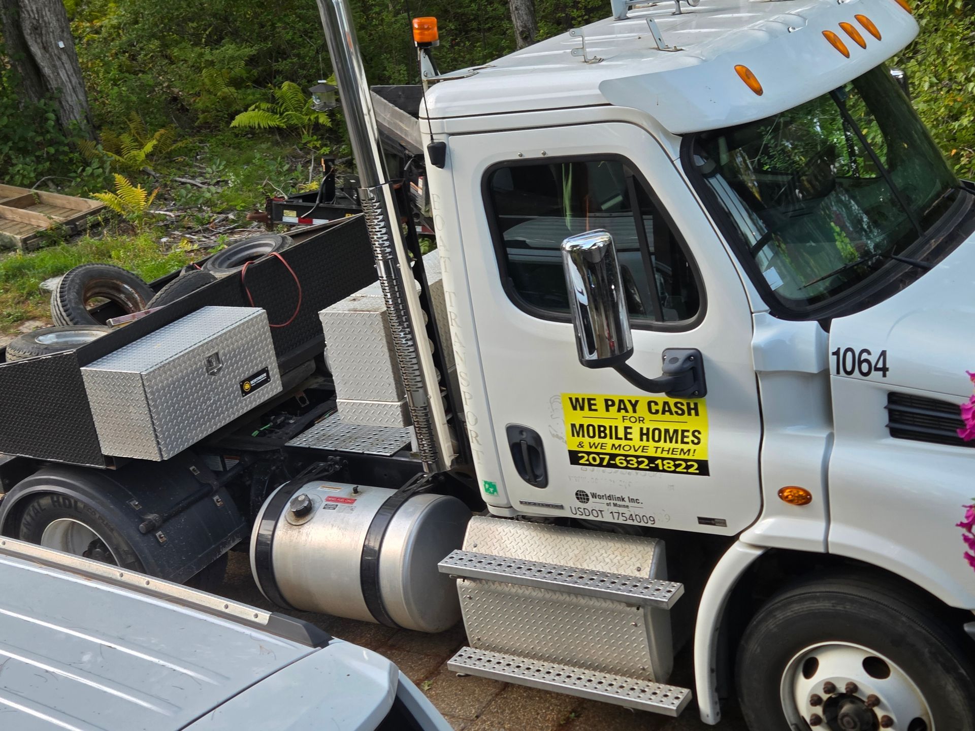 A white commercial tow truck parked outdoors, featuring a sign on the door advertising cash for mobile homes.