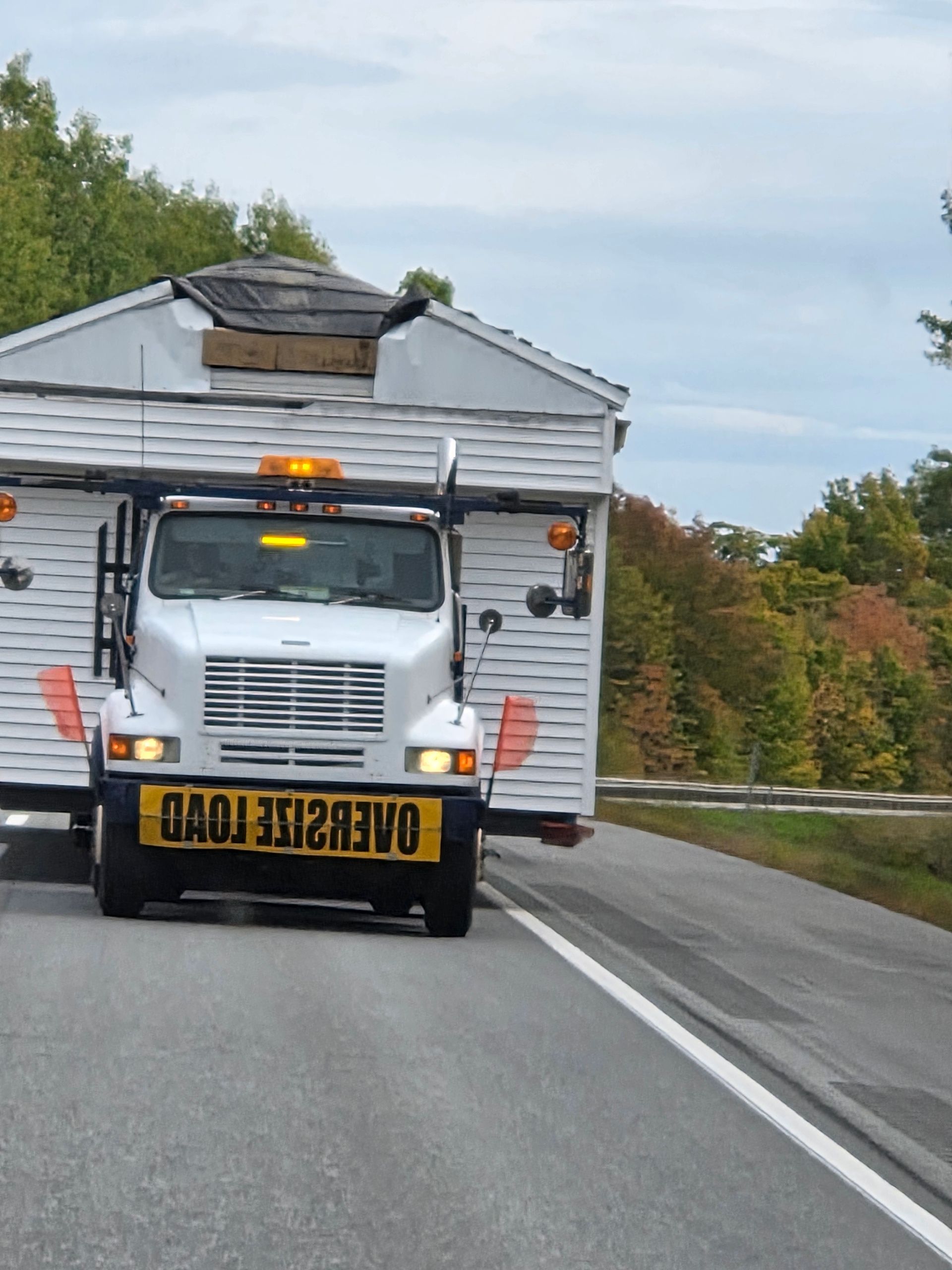 A white truck carrying a damaged mobile home structure with an 