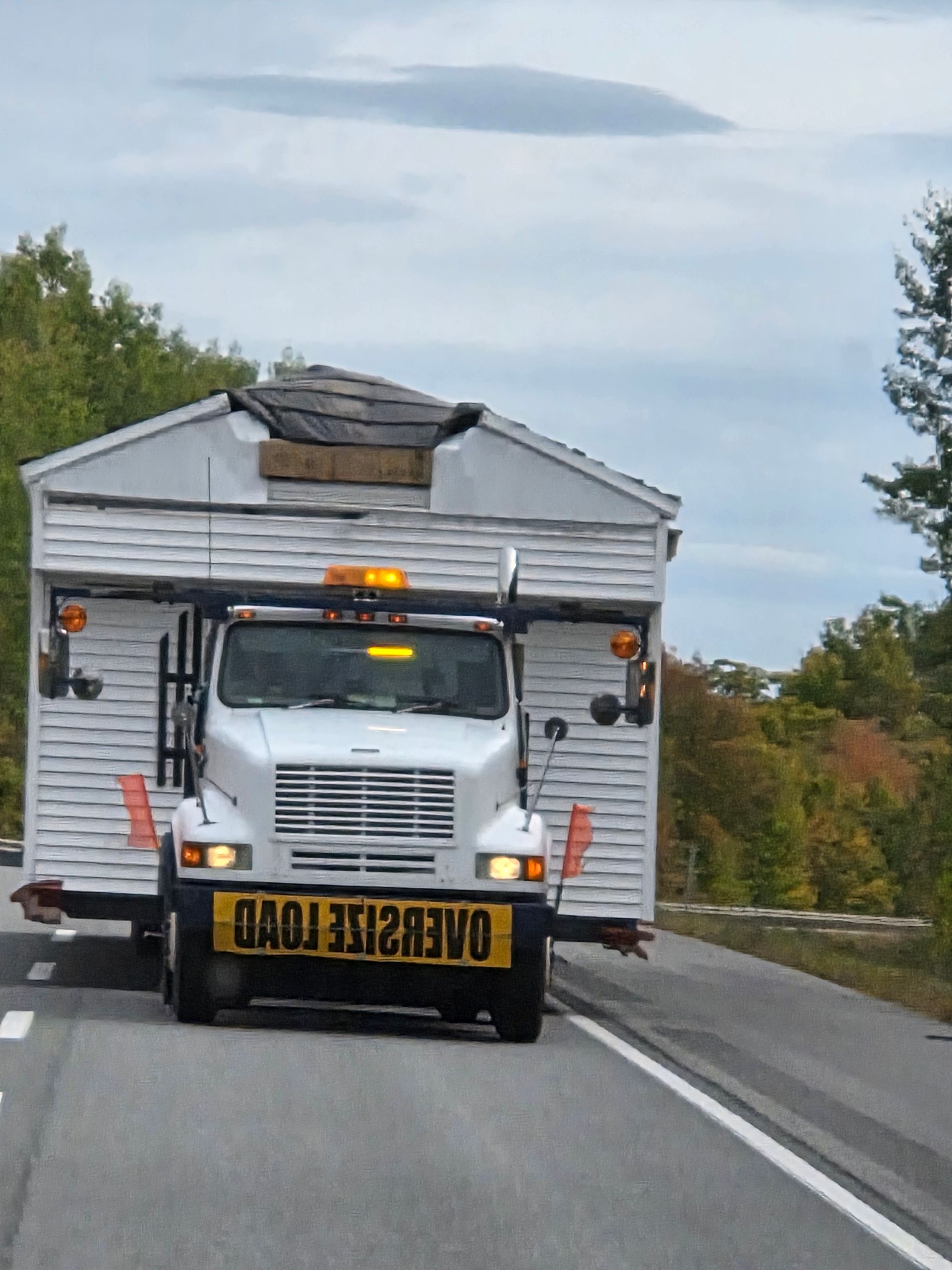 A white truck driving on a road, transporting a house with an 