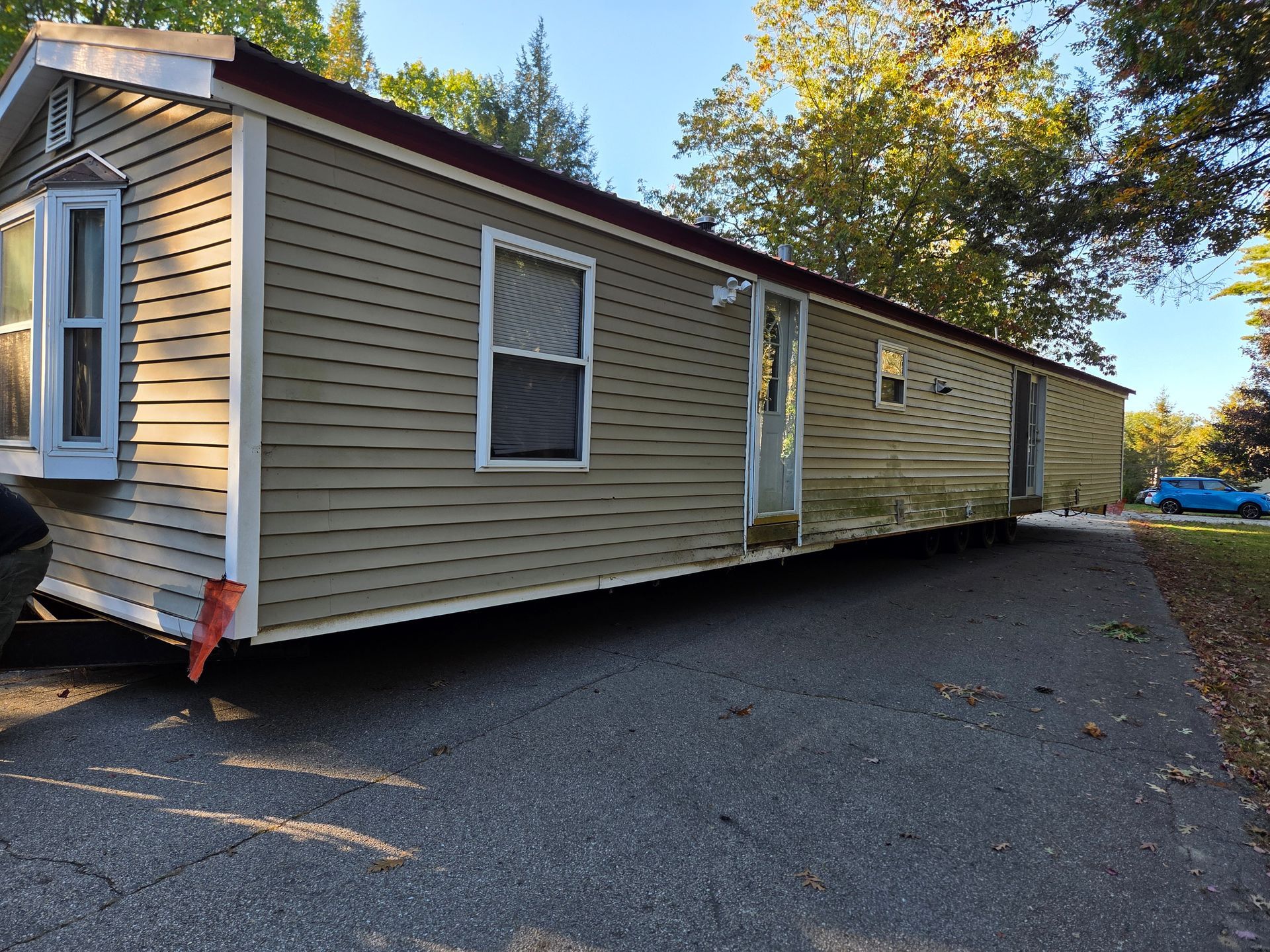 A tan mobile home with a bay window and multiple entrances, parked on an asphalt driveway during the daytime.