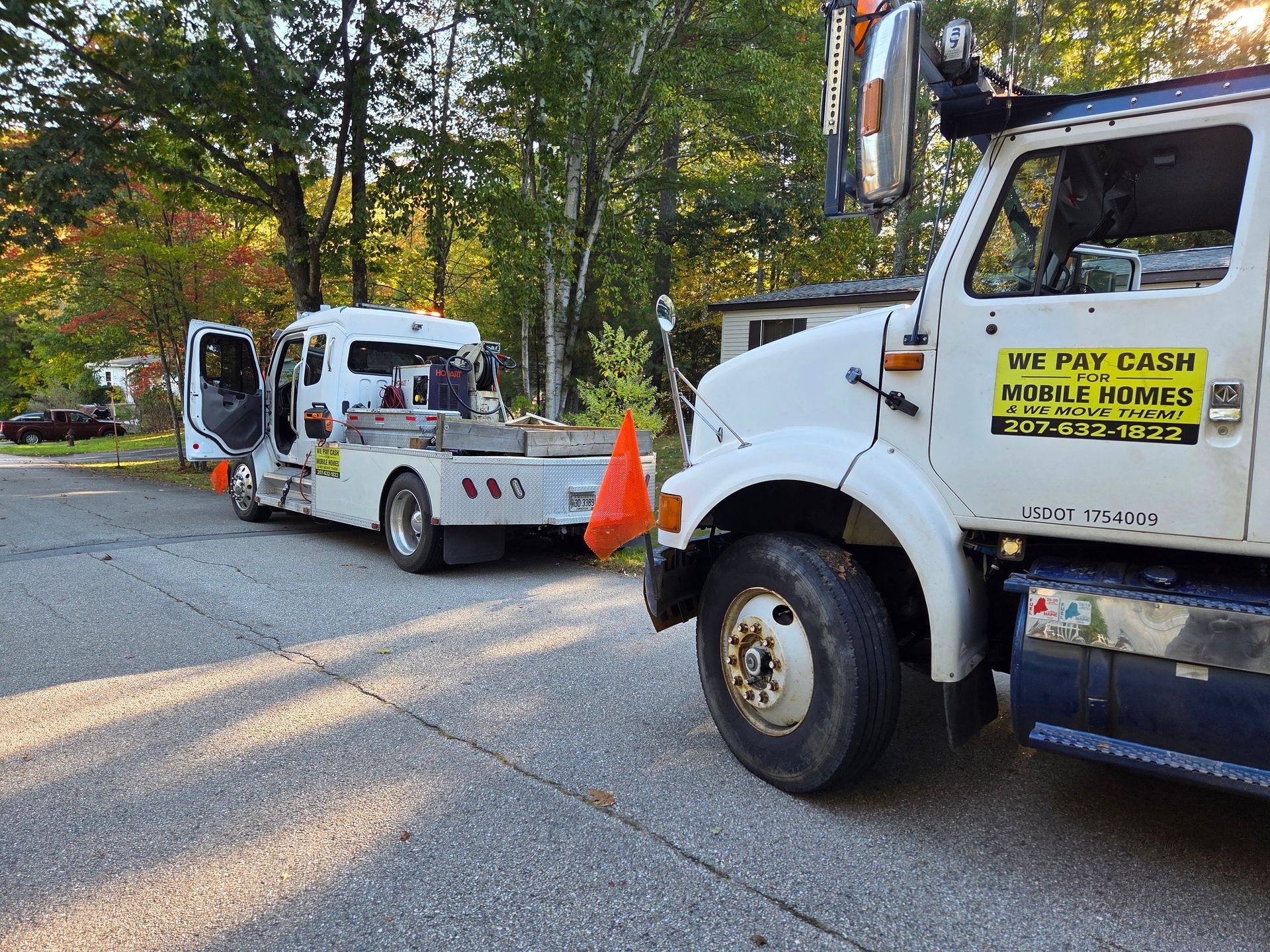 Two white commercial trucks parked on a paved road, with one showing a 