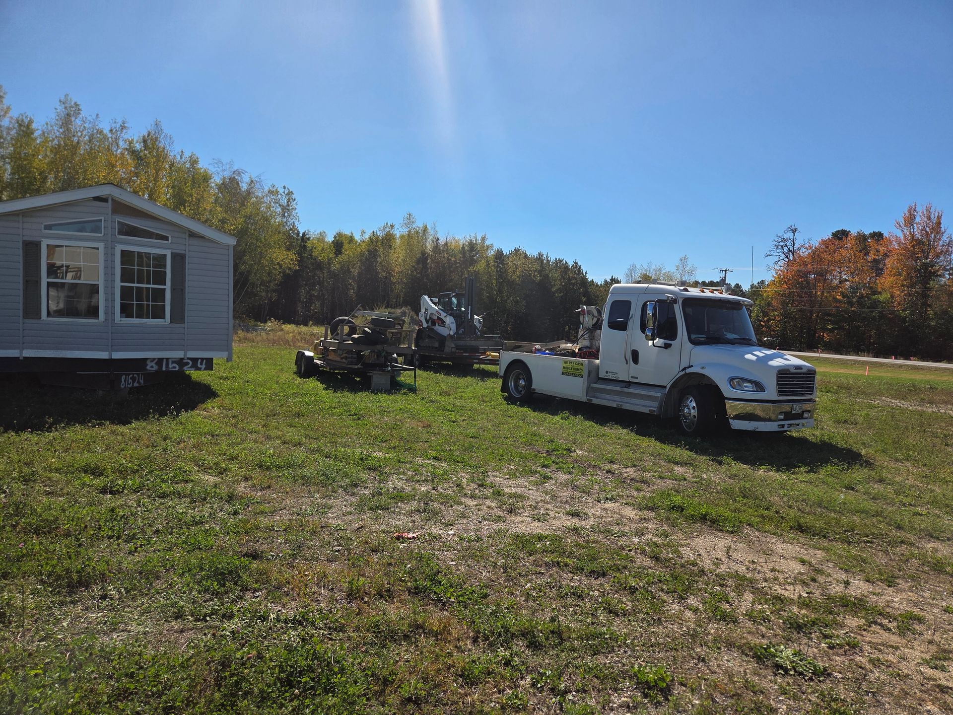 A modular home sits on a grassy field next to a white service truck and a piece of construction equipment.