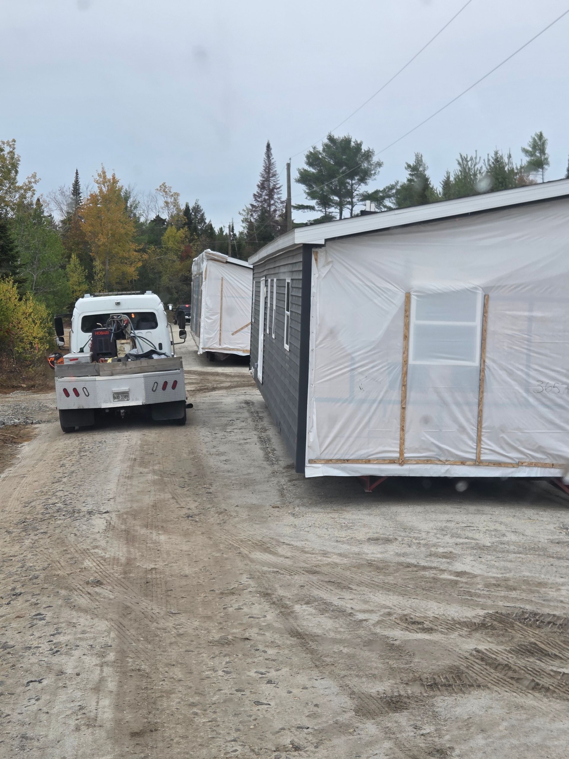 A truck parked on a gravel path next to two modular building sections wrapped in protective white plastic.