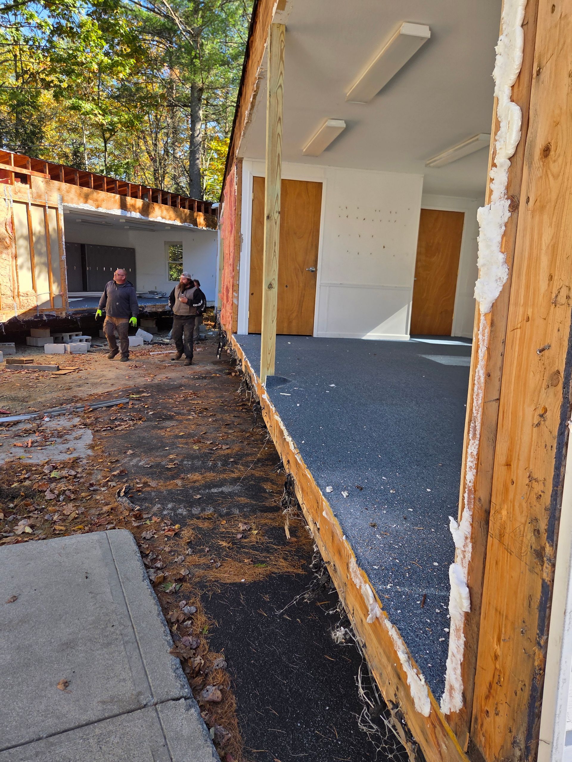 Two people work on a demolition site where a building's exterior wall has been removed, exposing the interior rooms.