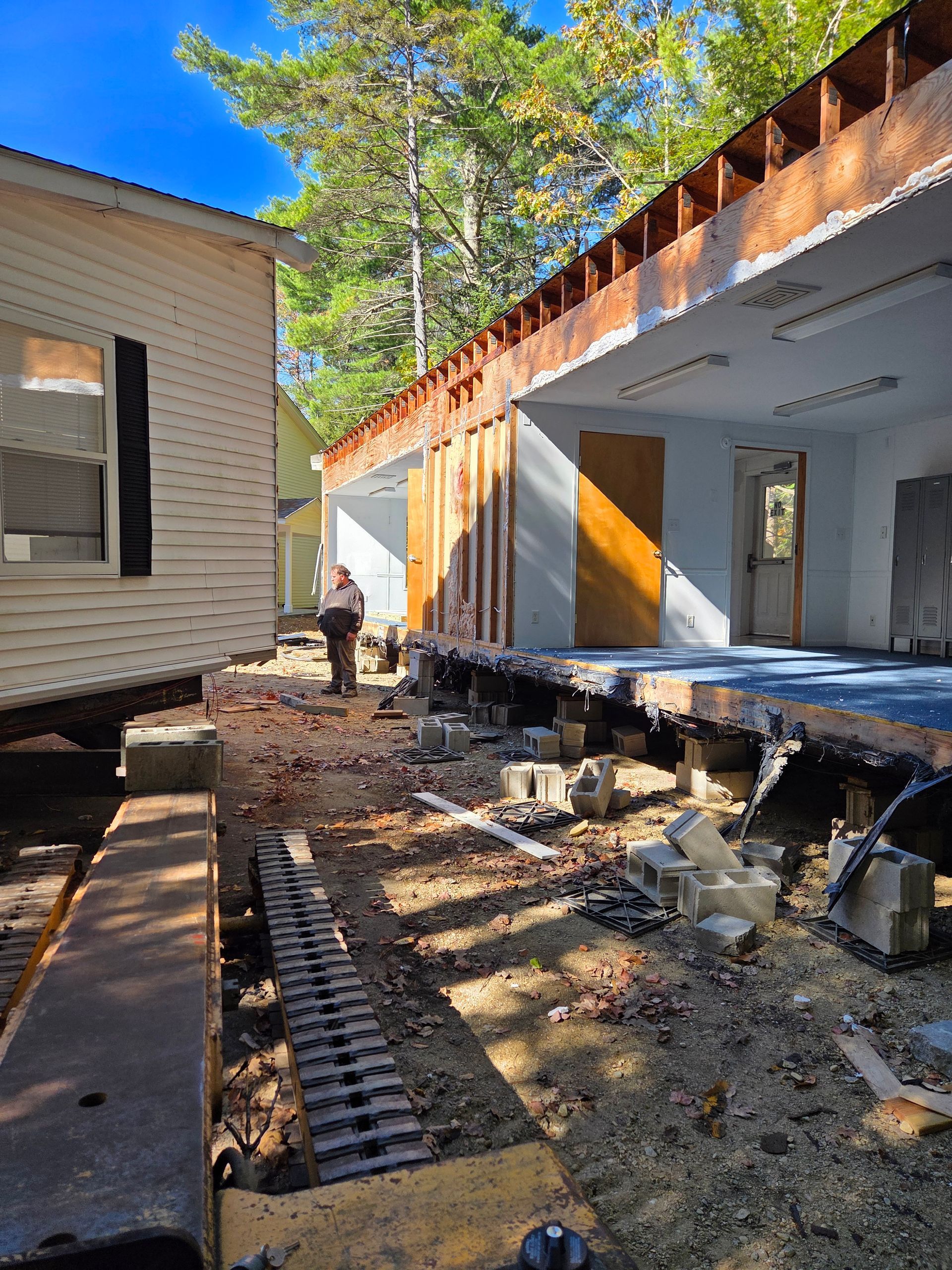 A person stands between two sections of a disassembled modular building on concrete block supports in a wooded area.