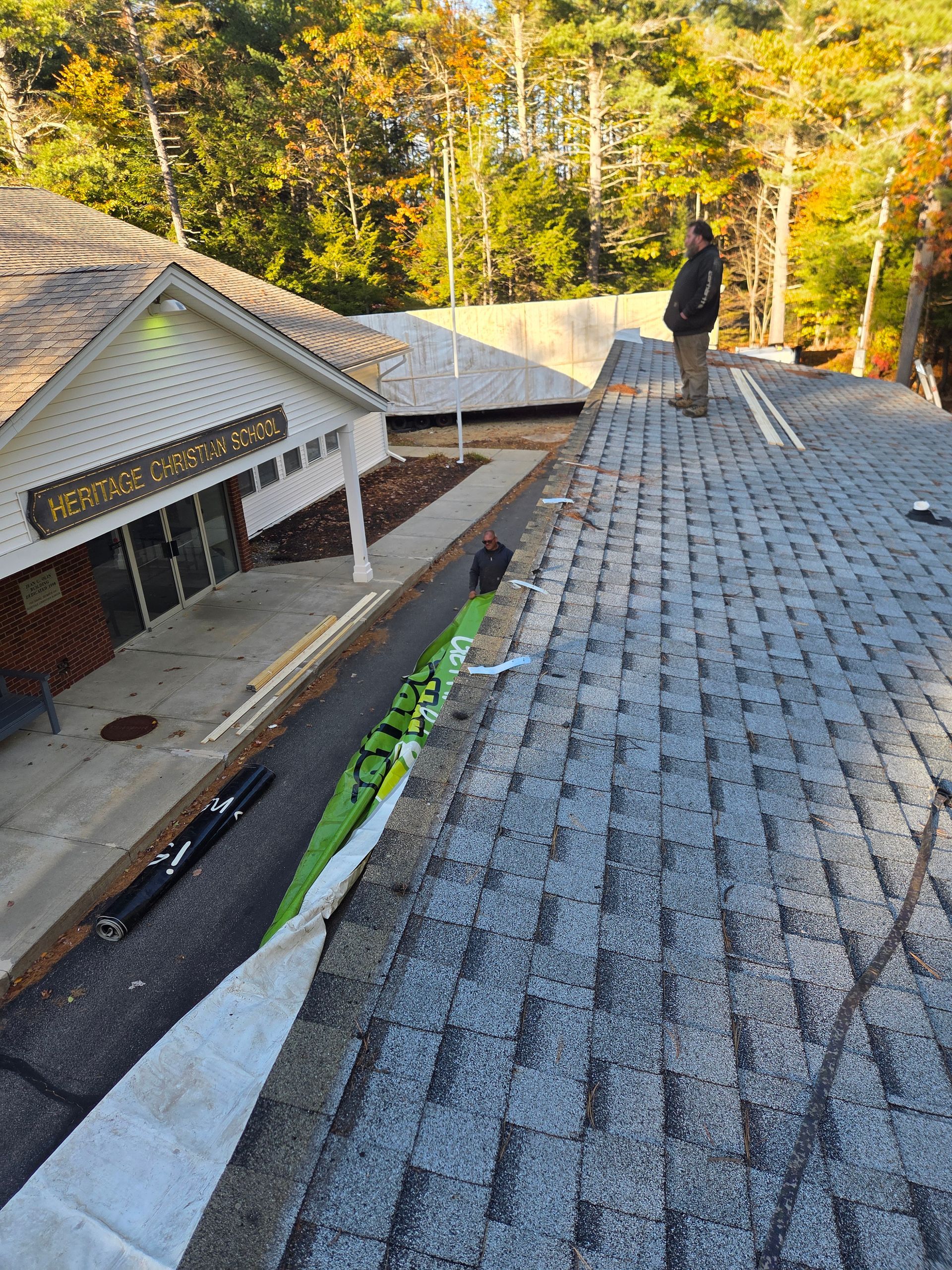 A person stands on a roof during construction, overlooking a building entrance with construction materials on the ground.