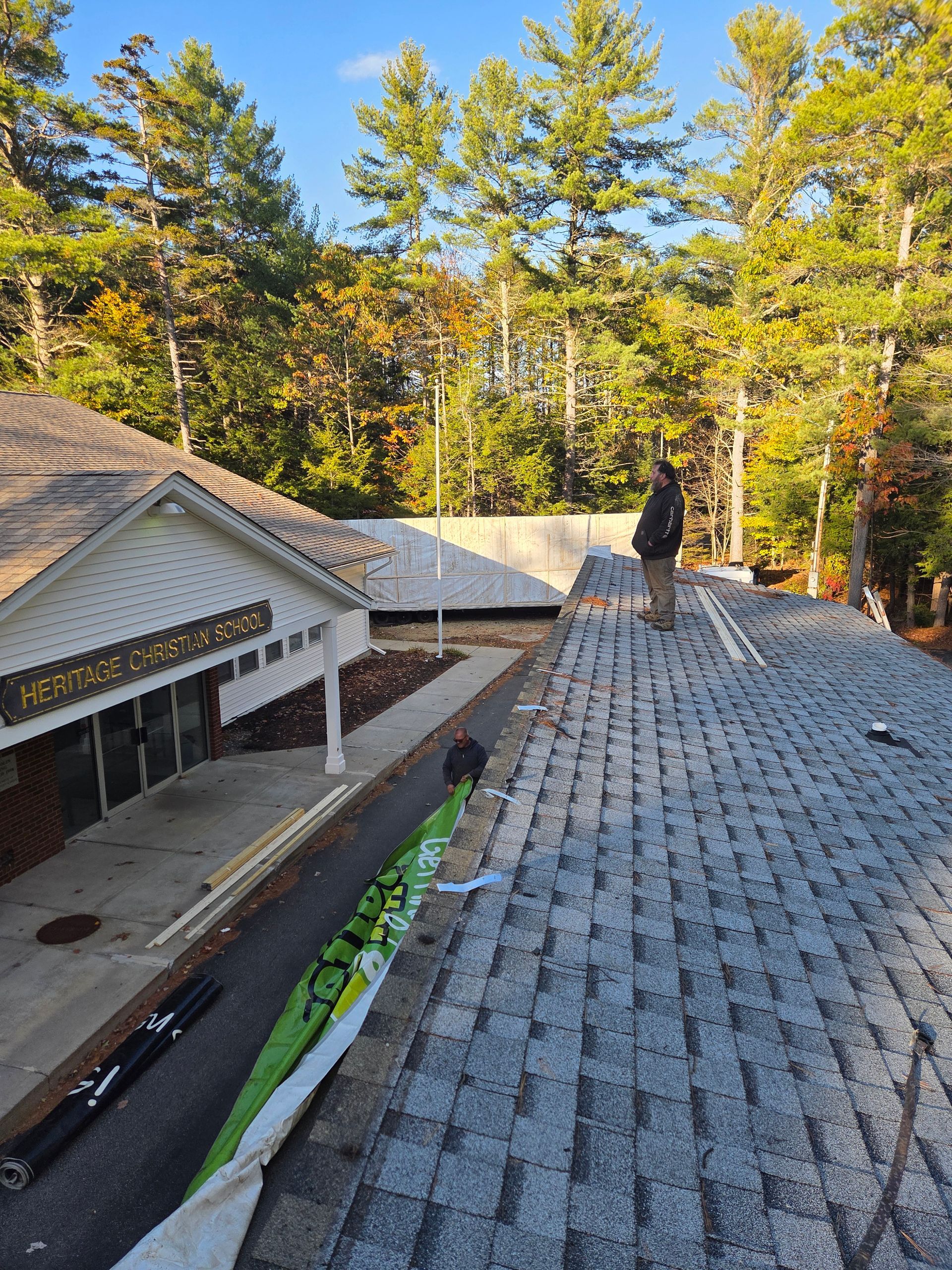 A worker stands on a residential roof during a renovation, with building materials and a construction area below.