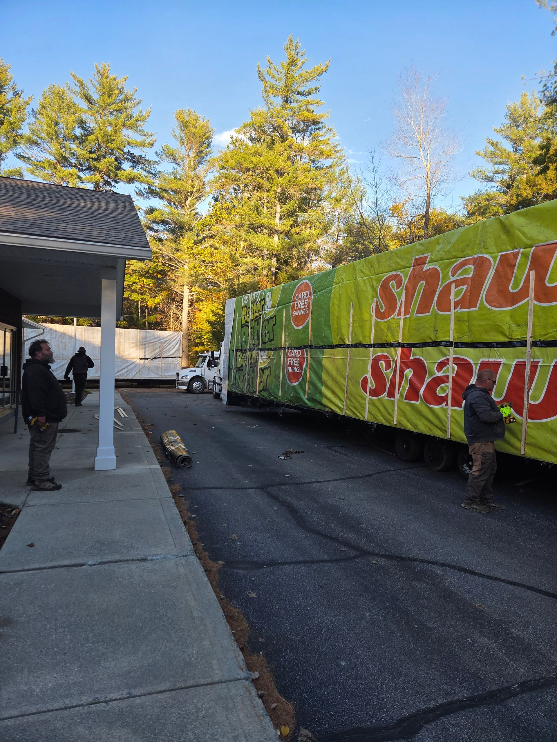 A Shaw carpet transport trailer parked on an asphalt road next to a building, with two people standing nearby.