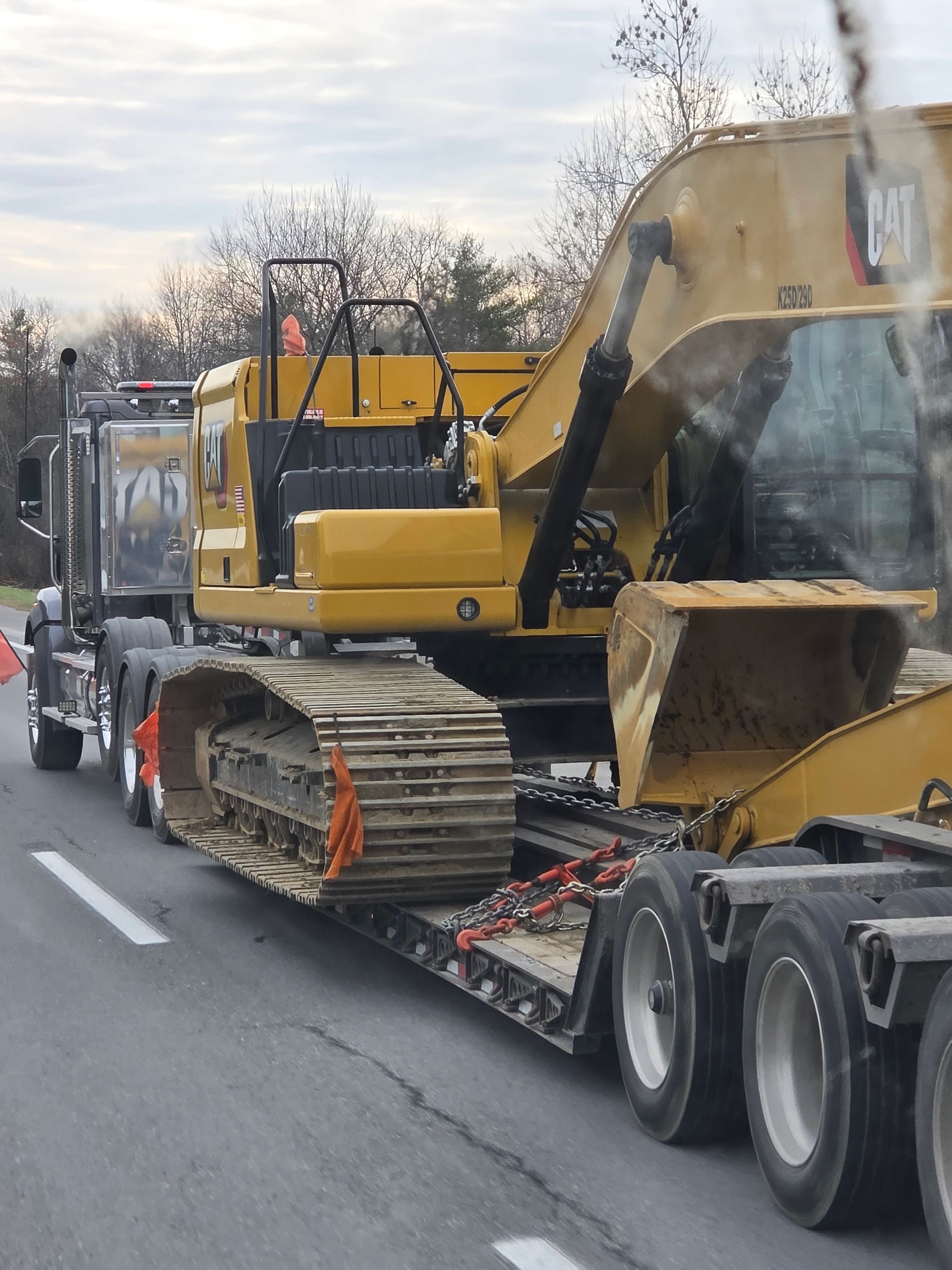 A yellow Caterpillar excavator being transported on a flatbed trailer pulled by a semi-truck on a road.