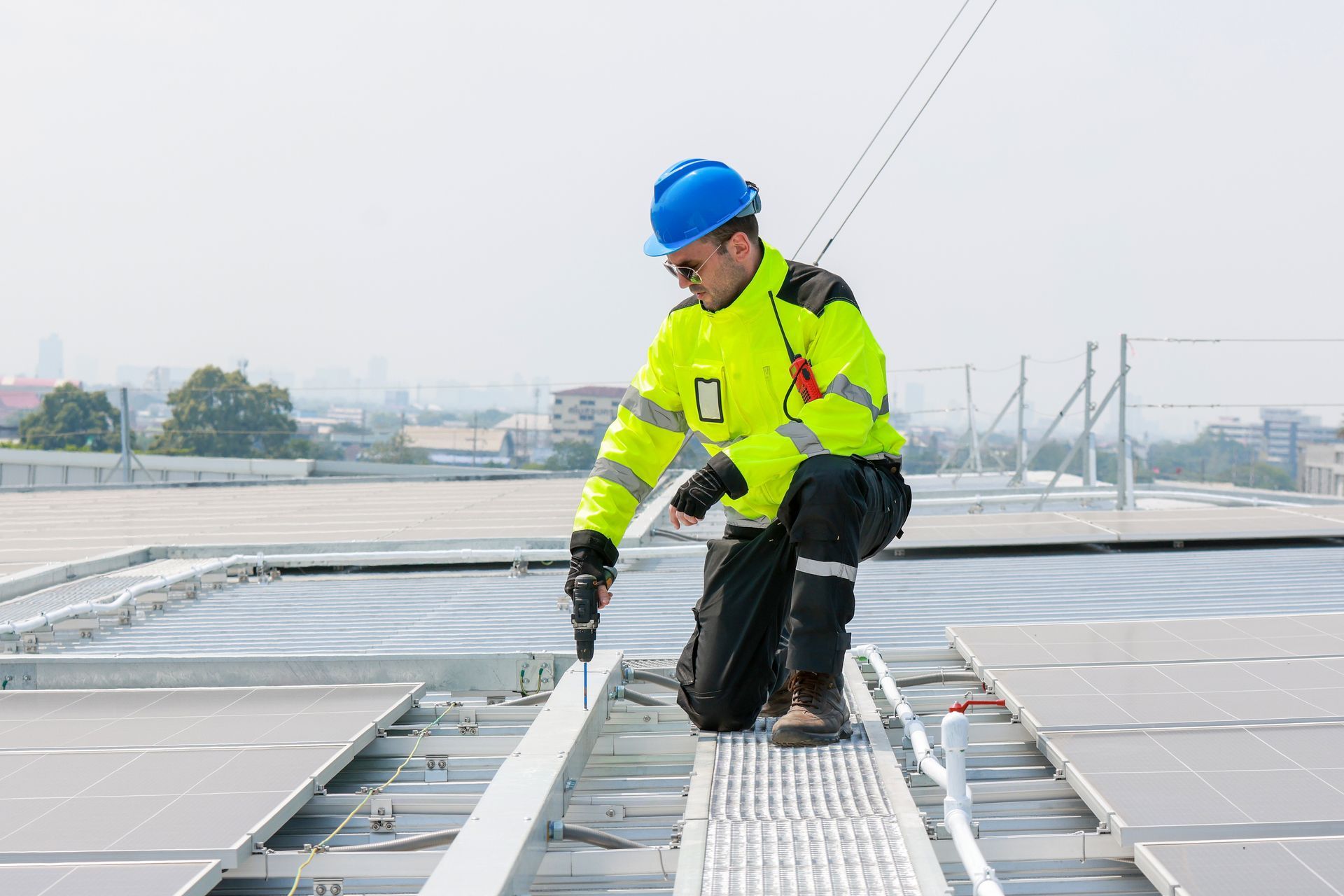 Worker in a blue hard hat and neon jacket inspecting rooftop solar panels.