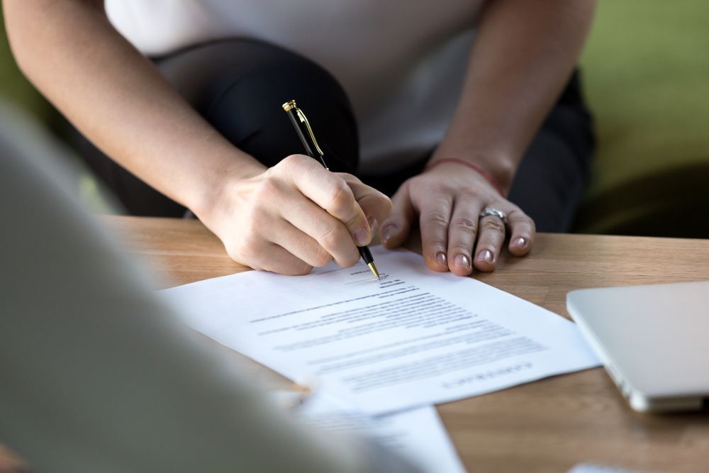A Woman Is Writing On A Piece Of Paper With A Pen — Bradley J Bragg - Solicitor in Atherton, QLD