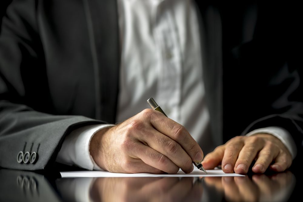 A Man In A Suit Is Writing On A Piece Of Paper With A Pen — Bradley J Bragg - Solicitor in Atherton, QLD