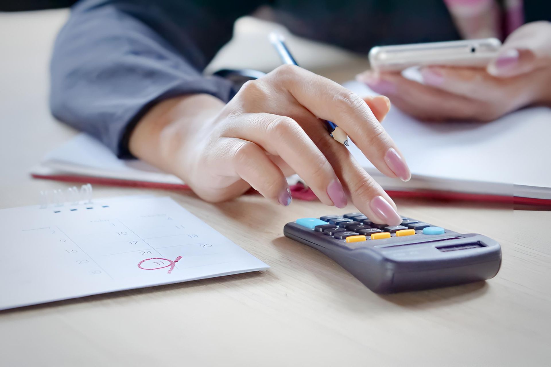 A Woman is Using a Calculator While Holding a Cell Phone — Bradley J Bragg - Solicitor in Atherton, QLD