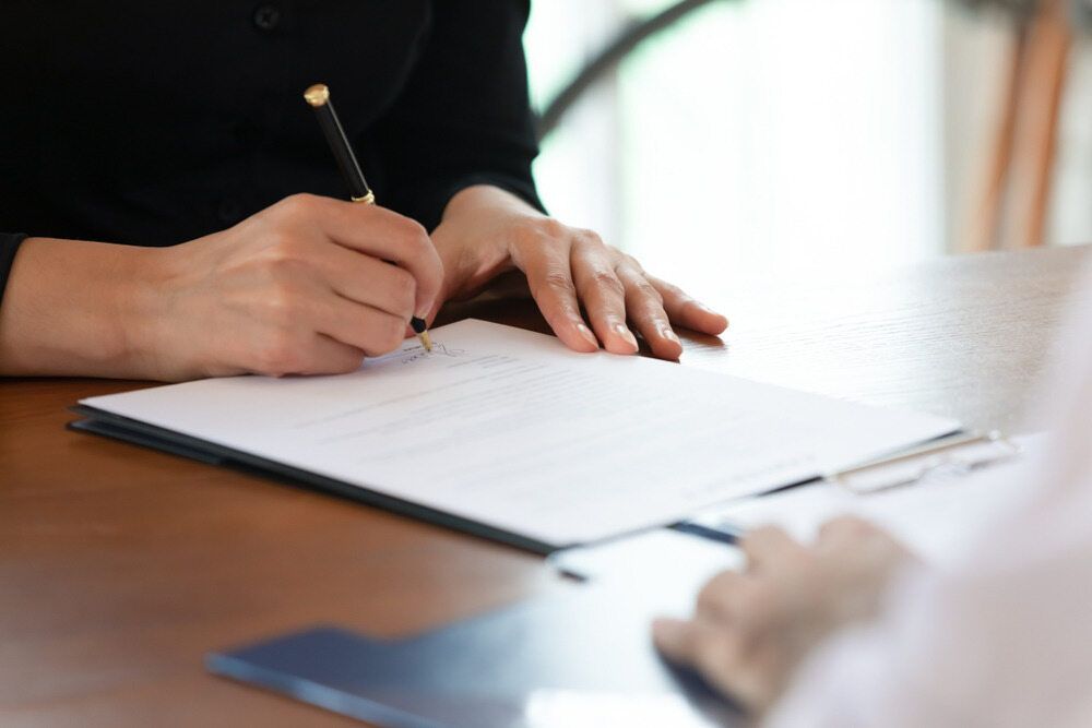 A Woman is Sitting at a Table Signing a Document With a Pen  — Bradley J Bragg - Solicitor in Atherton, QLD