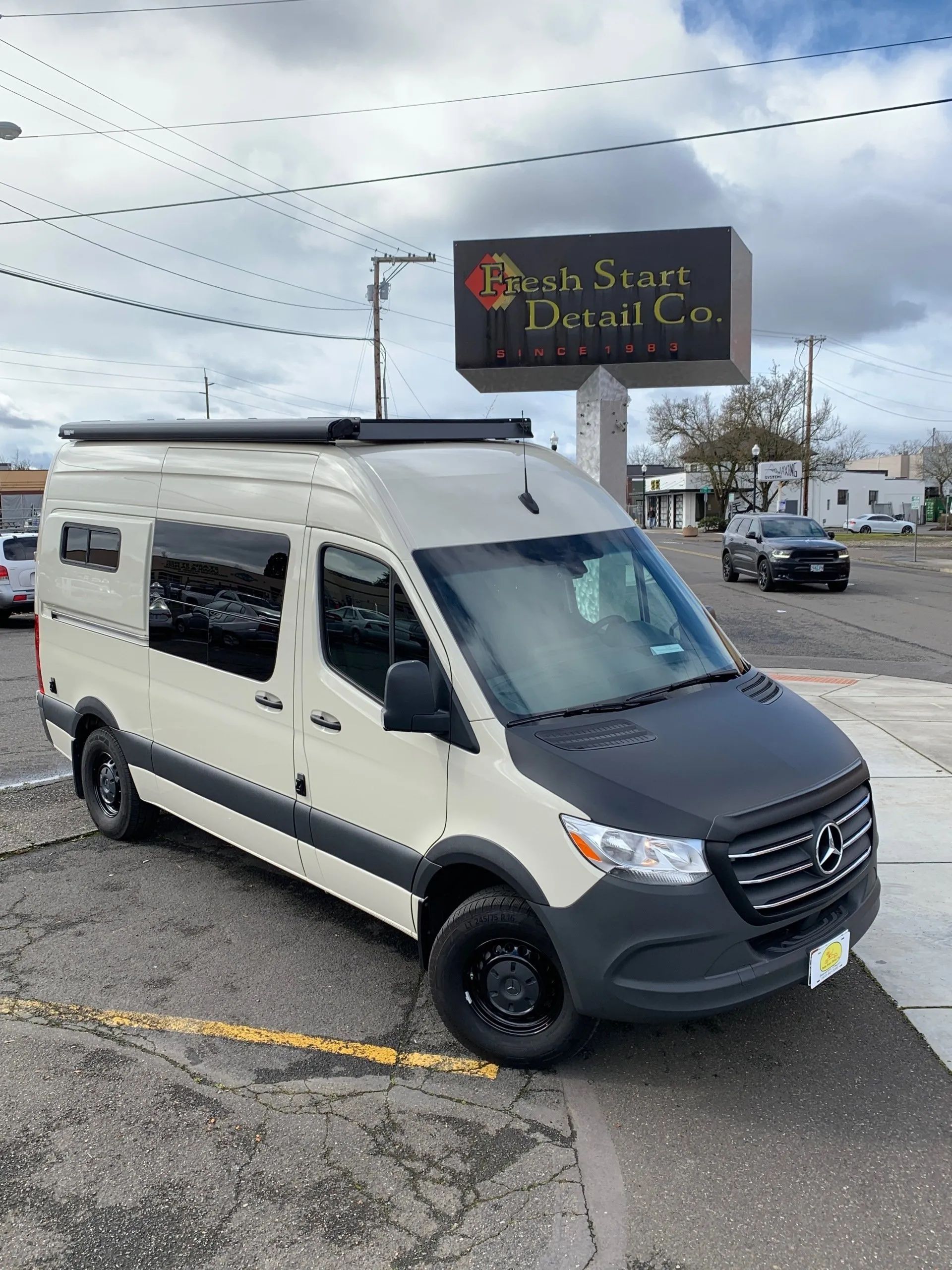 Cream and black camper van parked in front of a sign for 