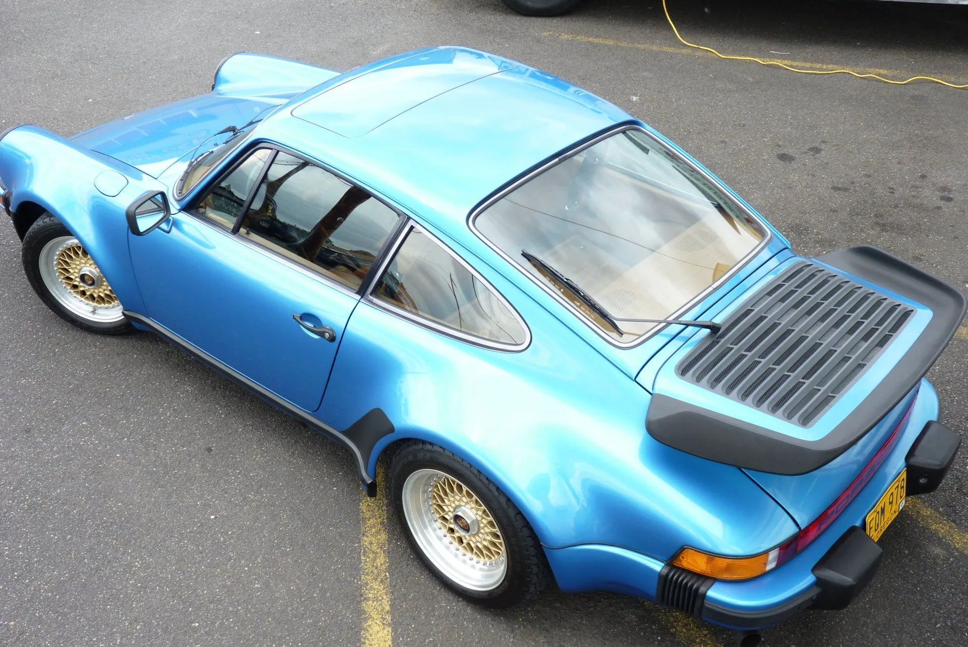 Blue Porsche 911, overhead shot. Classic sports car with gold wheels, parked on pavement.