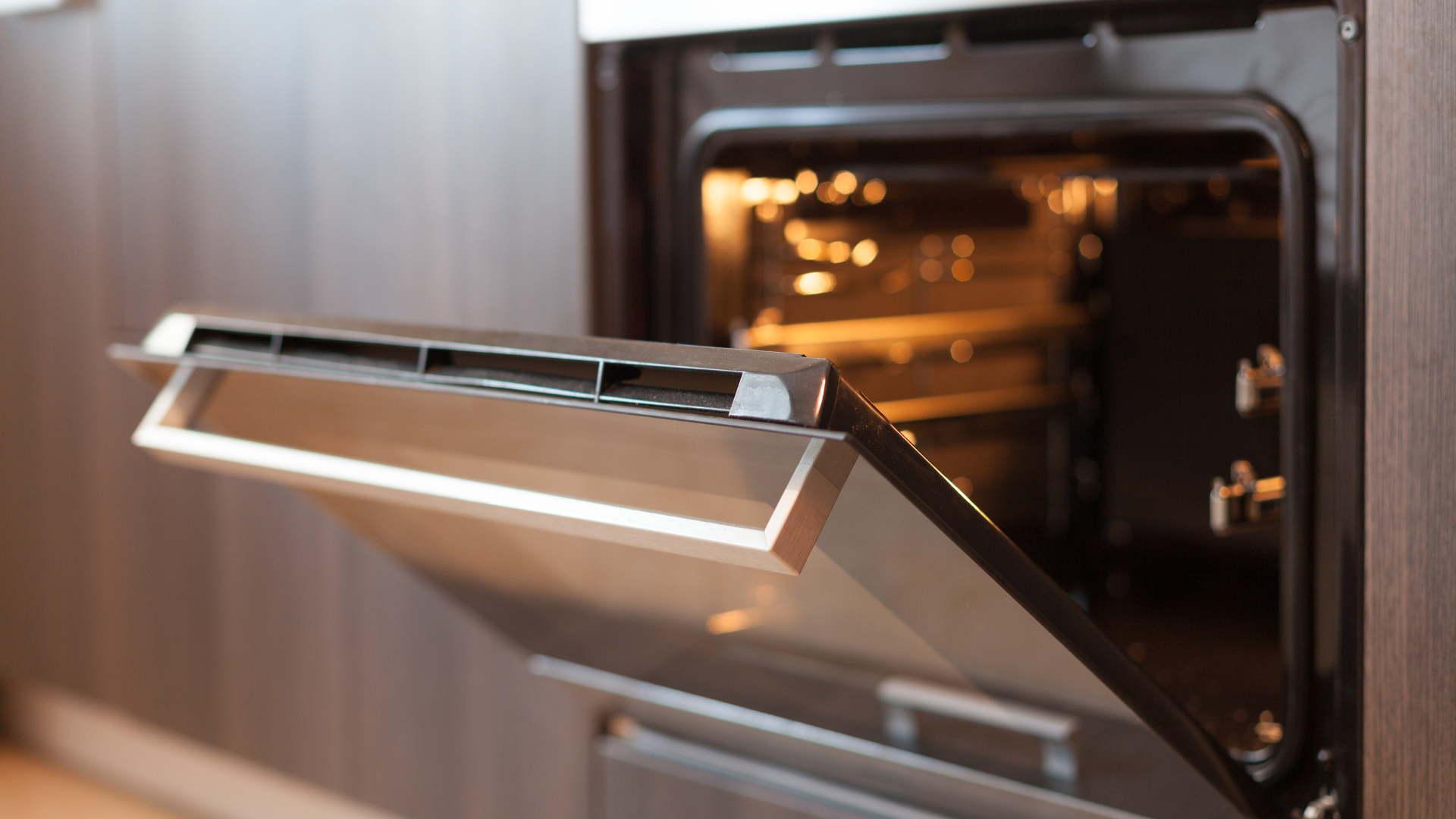 Open oven with interior light on, in a modern kitchen.