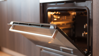 Open oven with interior light on, in a modern kitchen.