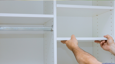 Person installing a white shelf in a closet.