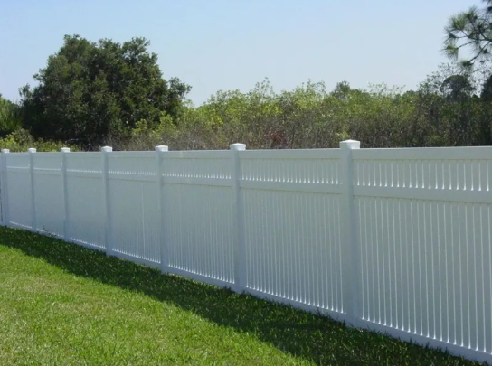 White vinyl privacy fence along a grassy yard with trees in the background