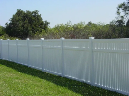 White vinyl fence along a grassy lawn with trees in the background