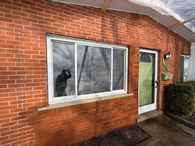 Brick house exterior with white-trimmed window, green door, and snow on the roof overhang