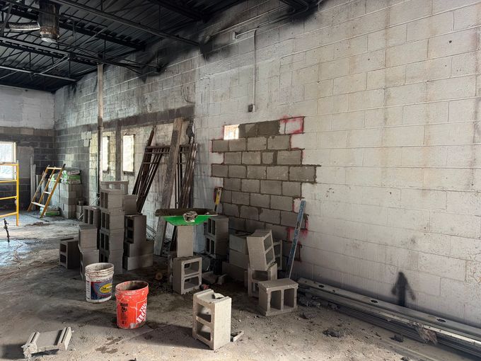 Partially built cinder block wall inside a construction site with tools, buckets, and scaffolding from a dusty floor