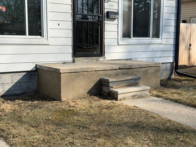 Front porch with concrete steps and a black door on a white house exterior