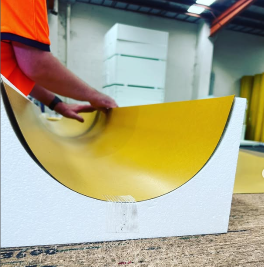 A man in an orange shirt is holding a yellow piece of cardboard