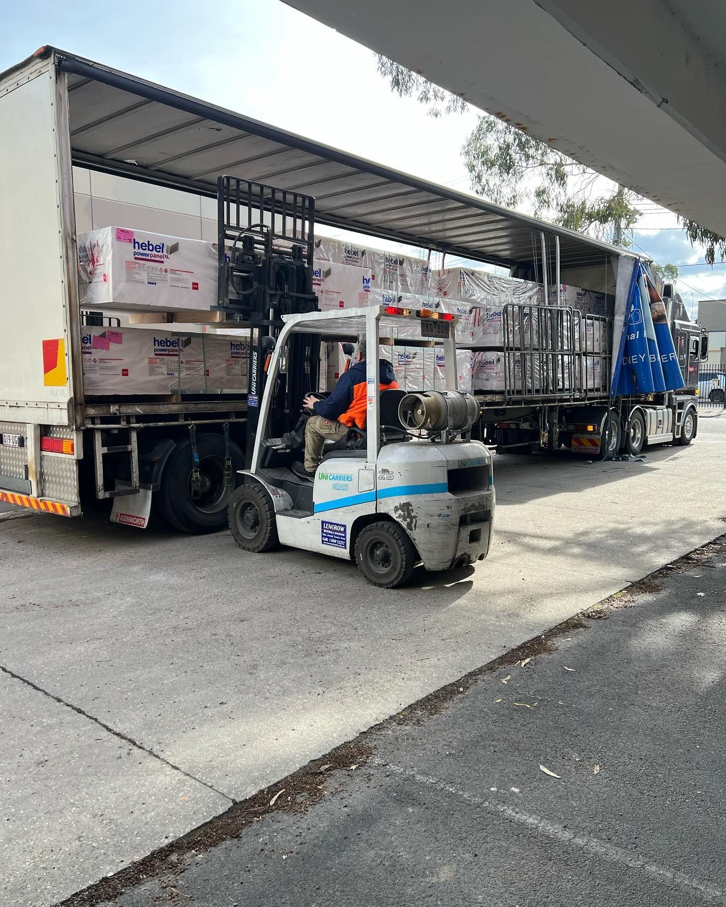A man is driving a forklift next to a truck.