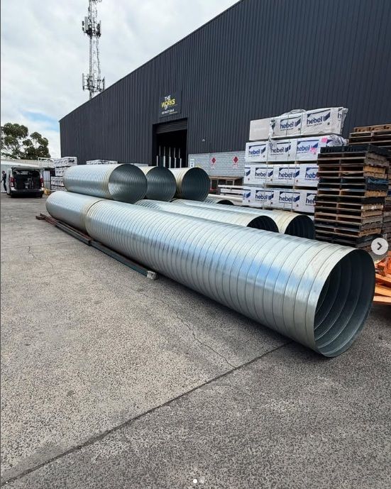 A bunch of metal pipes are stacked on top of each other in front of a building.