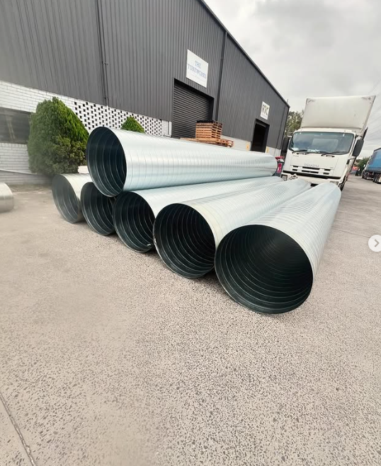 A bunch of metal pipes are stacked on top of each other in front of a building.