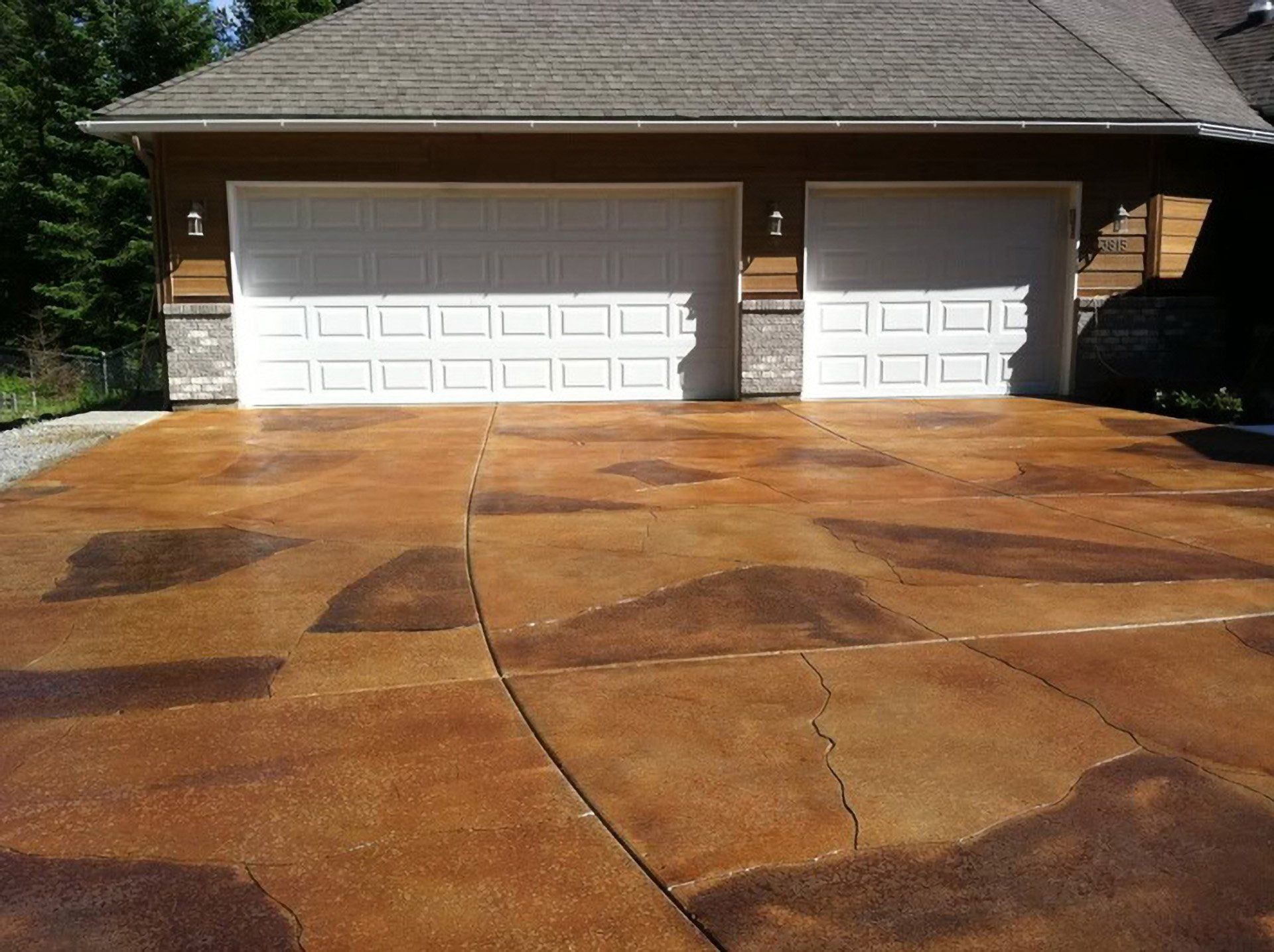 Two-car garage with white doors and a stained concrete driveway in front of a house