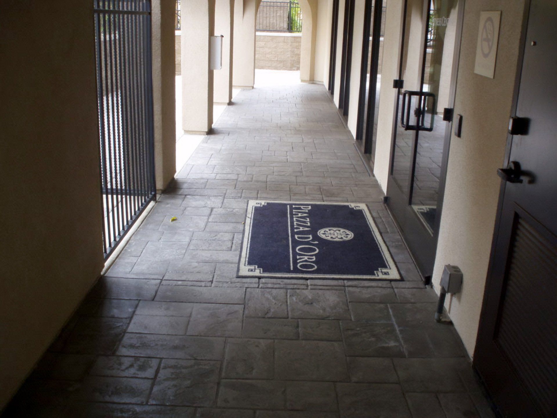 Covered outdoor corridor with stamped concrete floor and a welcome mat near apartment doors
