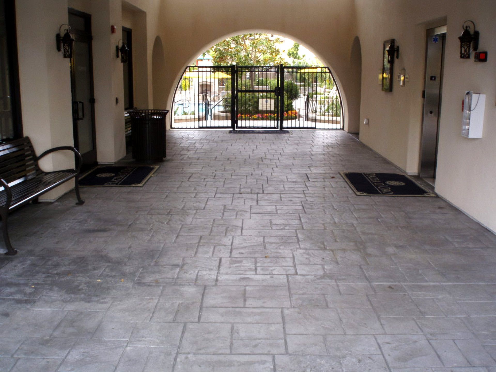 Covered walkway with stamped concrete floor leading to a gated courtyard in the distance
