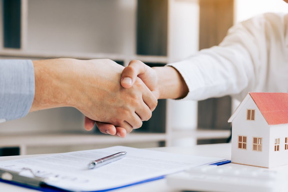 Two People Shaking Hands Over a Contract and a Small House Model — Trapski Family Law Geelong in Newtown, VIC