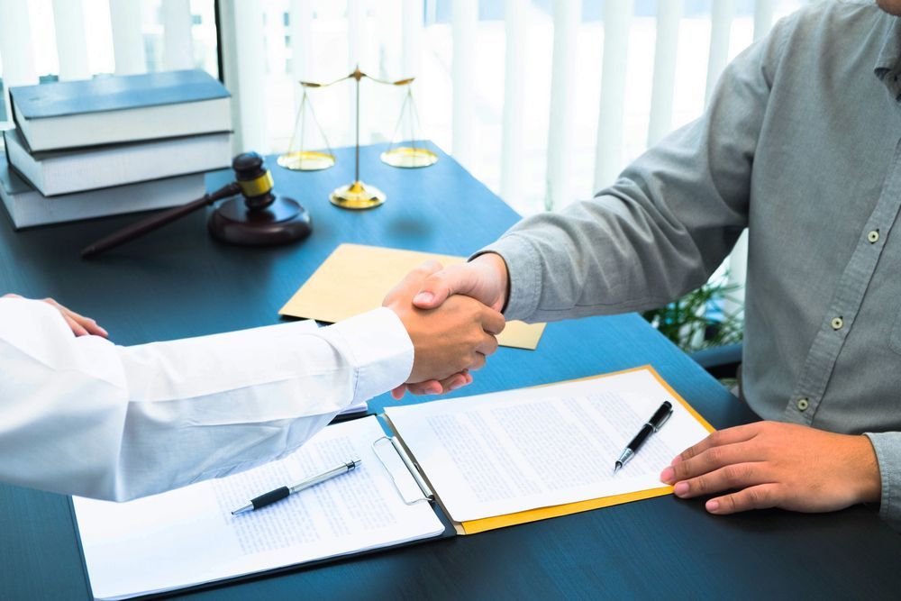 Two People Shaking Hands Over a Table With Legal Documents — Trapski Family Law Geelong in Newtown, VIC