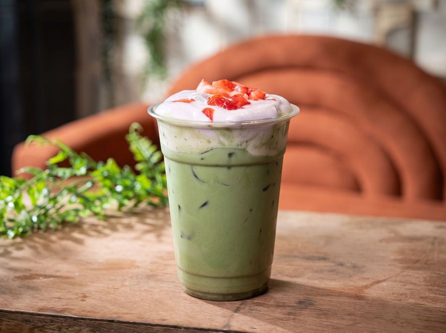 Iced green drink topped with whipped cream and strawberry bits on a wooden table
