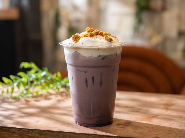 Iced purple drink with whipped cream and cinnamon on a wooden table near a window